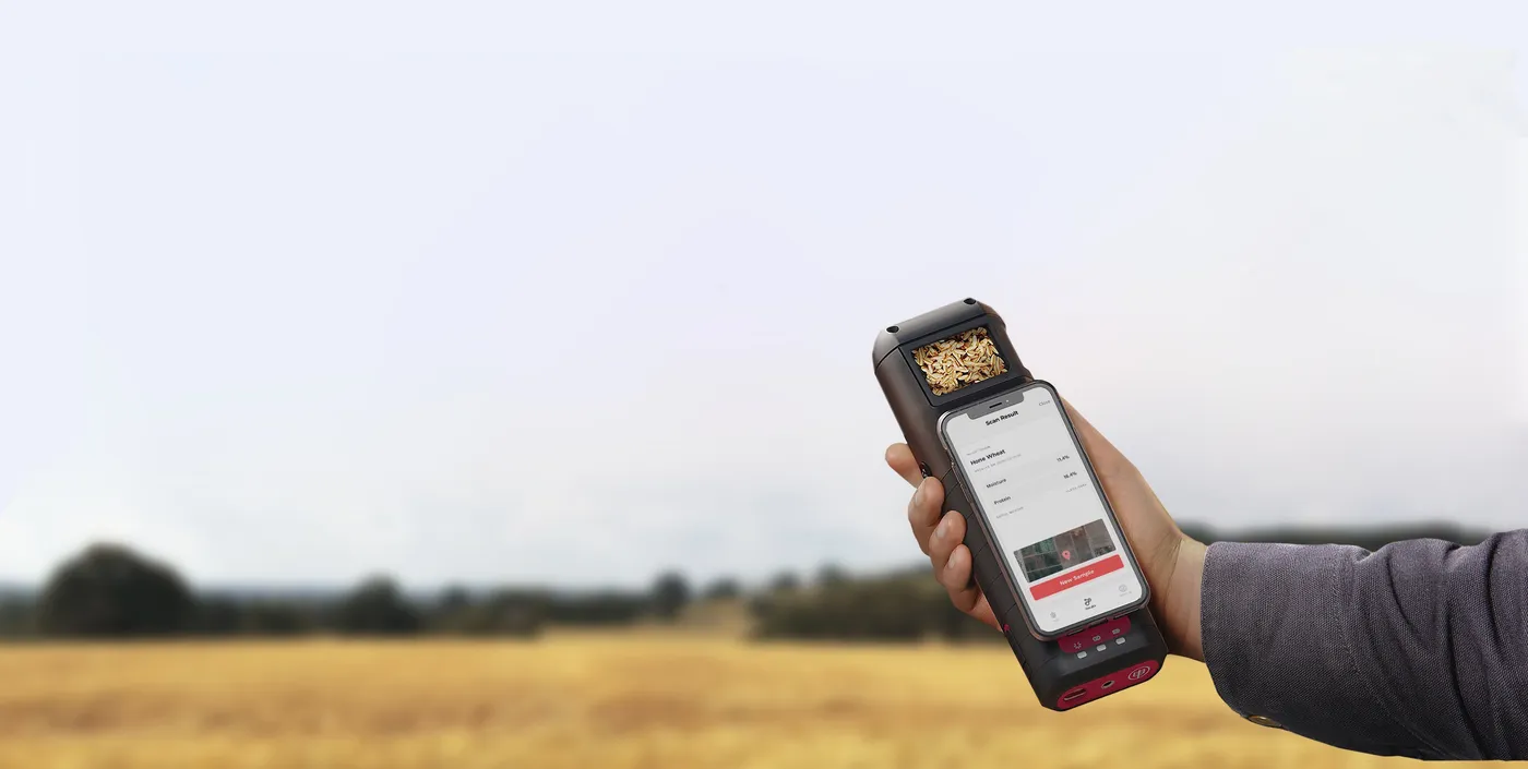 A grower holding up the Hone Lab Red in a wheat paddock, with moisture and protein results on the phone