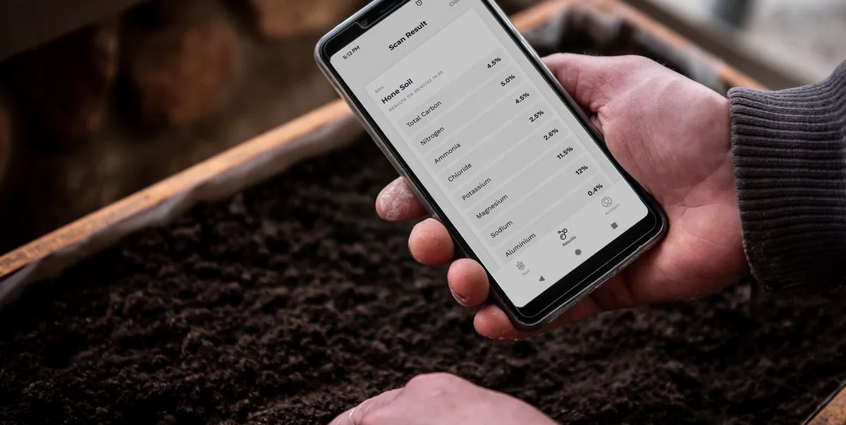 A phone showing total organic carbon results held above a freshly dug soil pit