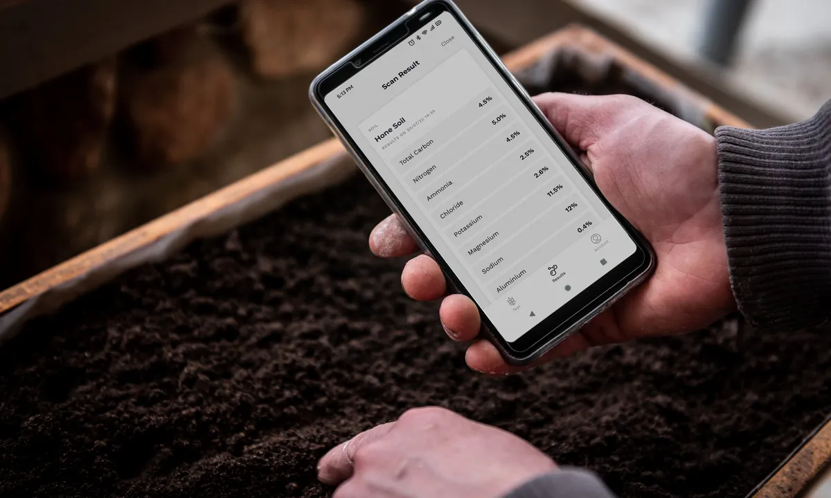 A phone showing total organic carbon results held above a freshly dug soil pit