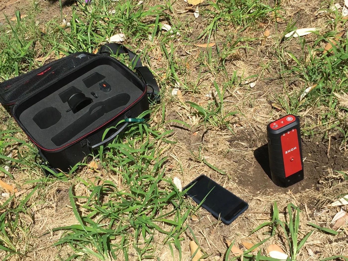 A Hone soil sampling kit open on the ground beside a Lab Red and a phone